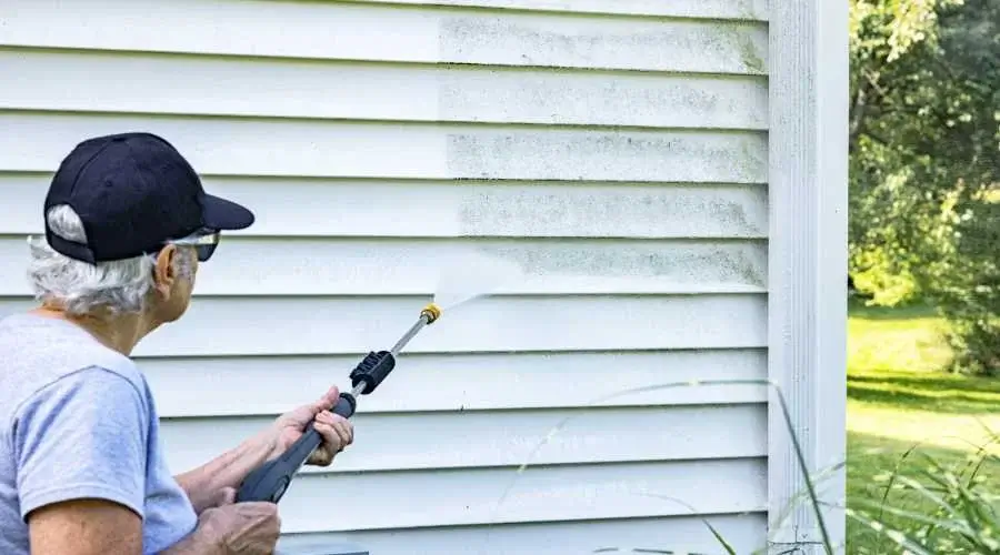 A person power washing mold off of the side of a house