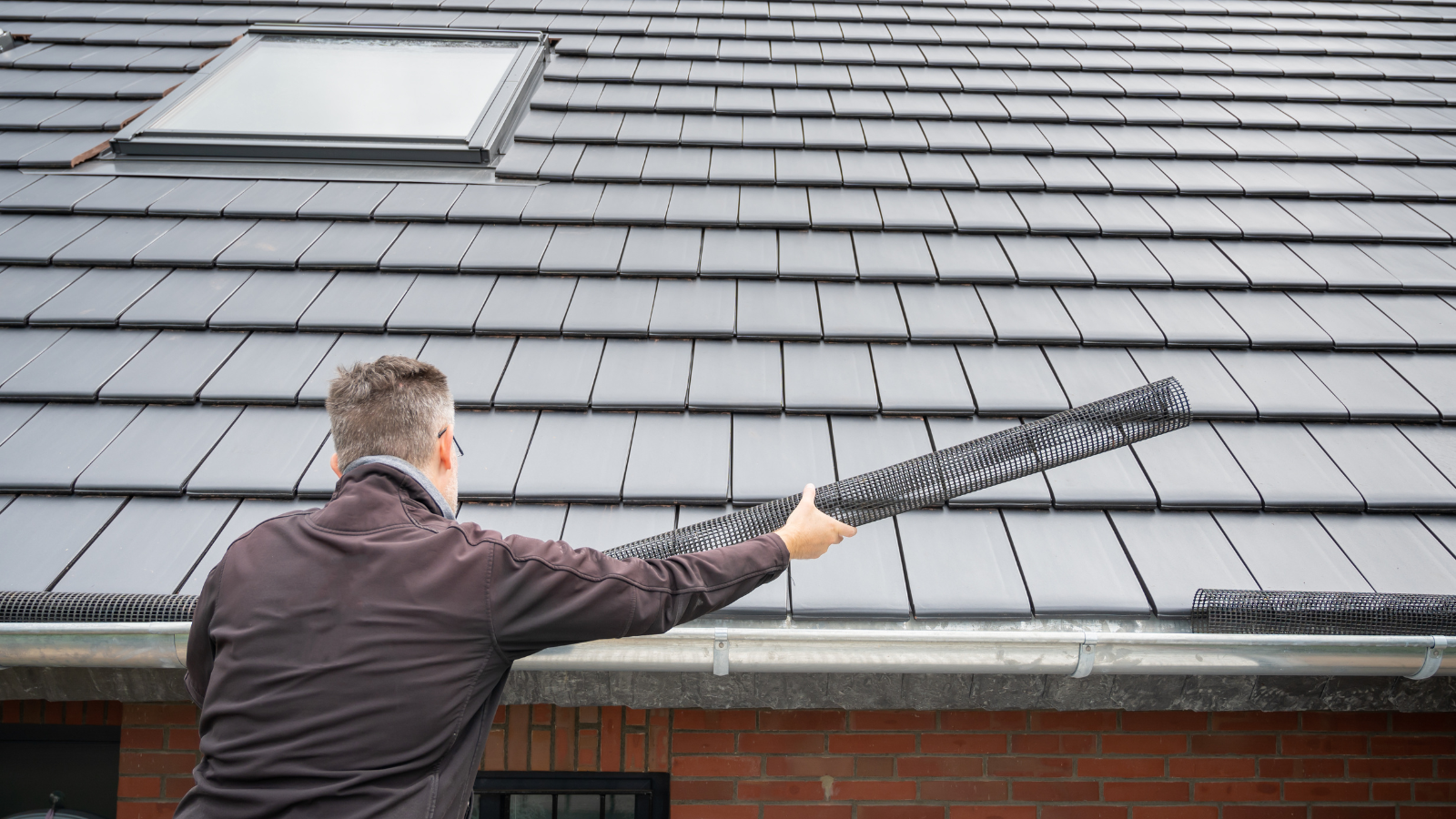 Person on a ladder putting gutter screens on a gutter