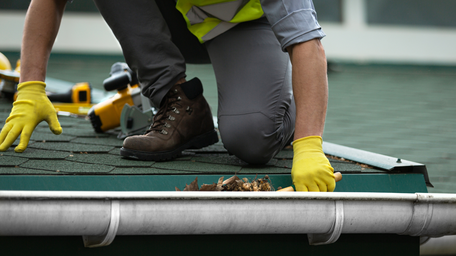 Person scooping debris out of a gray gutter on a roof