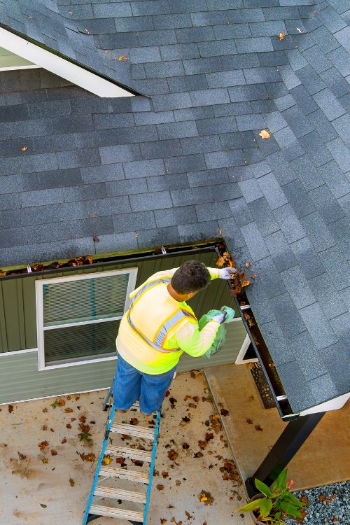 Man standing on a ladder cleaning leaves out of gutters
